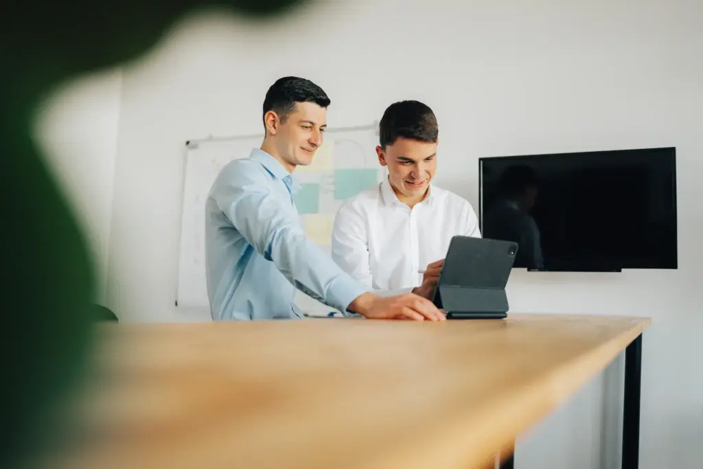 Berater von Blobel Consulting, einer in einem blauen Hemd, arbeiten gemeinsam an einem Tablet in Augsburg, symbolisieren Teamarbeit und digitale Vertriebskompetenz.